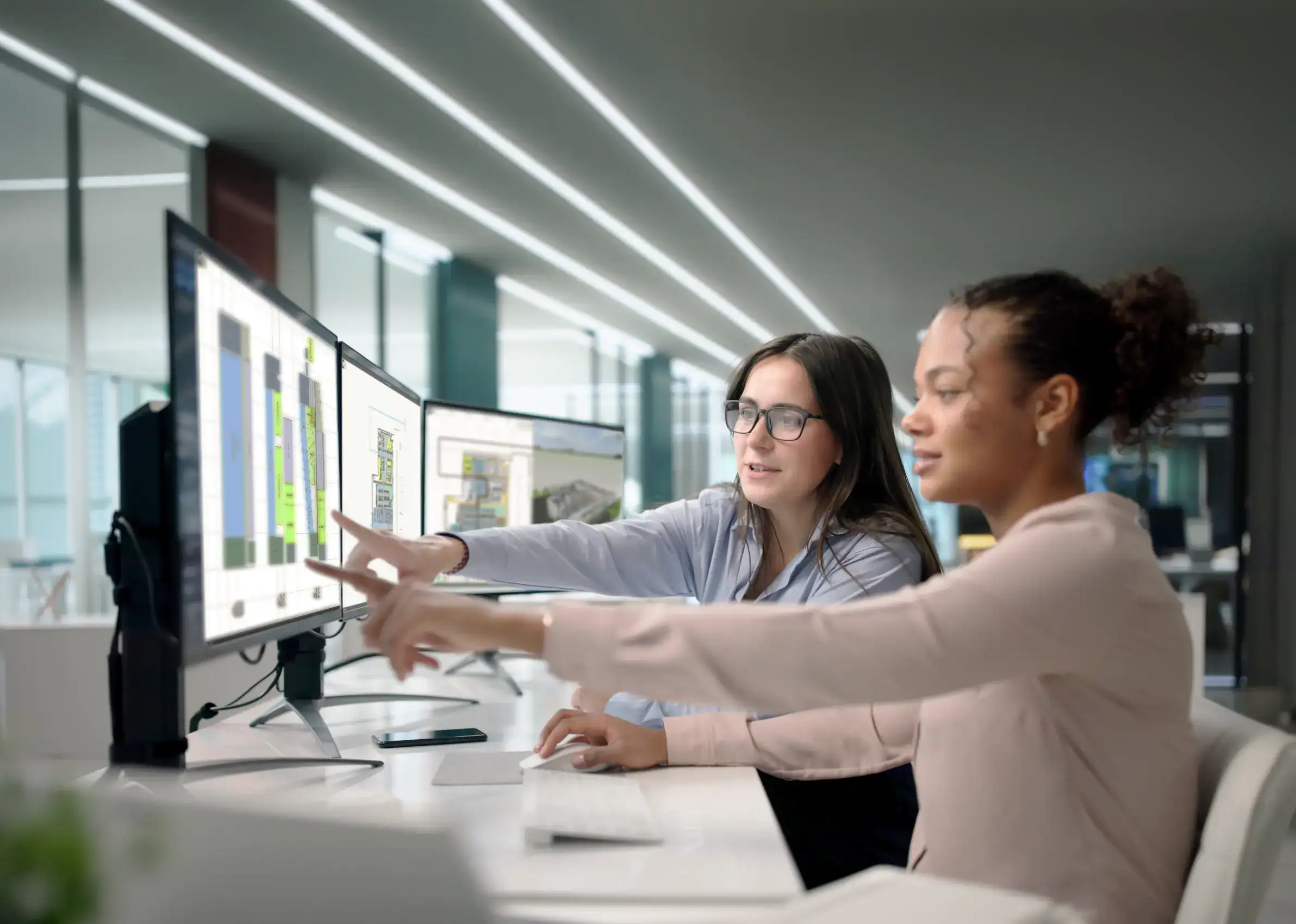 Zwei Frauen sitzen vor mehreren Monitoren und arbeiten an Layouts in visTable