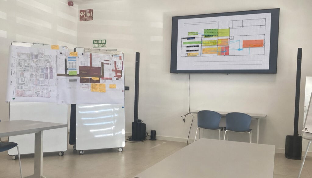 Workshop room with printed layout plans on whiteboards and a digital factory layout on a screen
