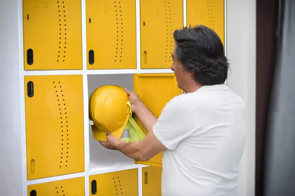 worker removes helmet from locker in factory locker room