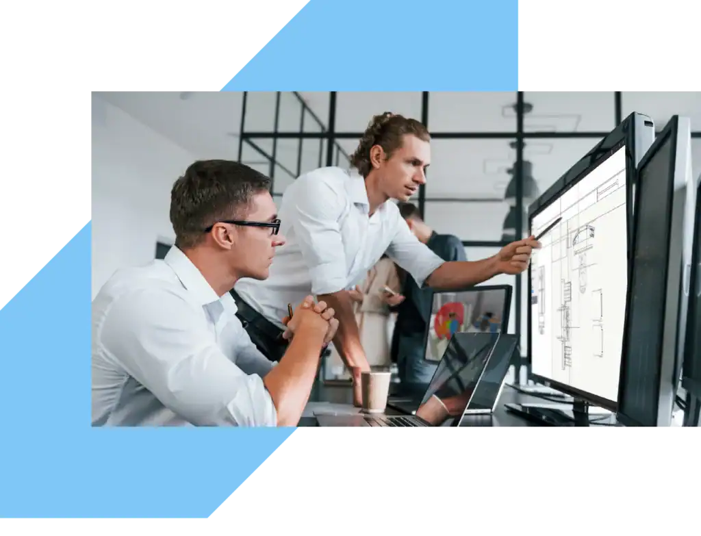 2 men are standing at the desk. one is pointing at the floor plan on a monitor