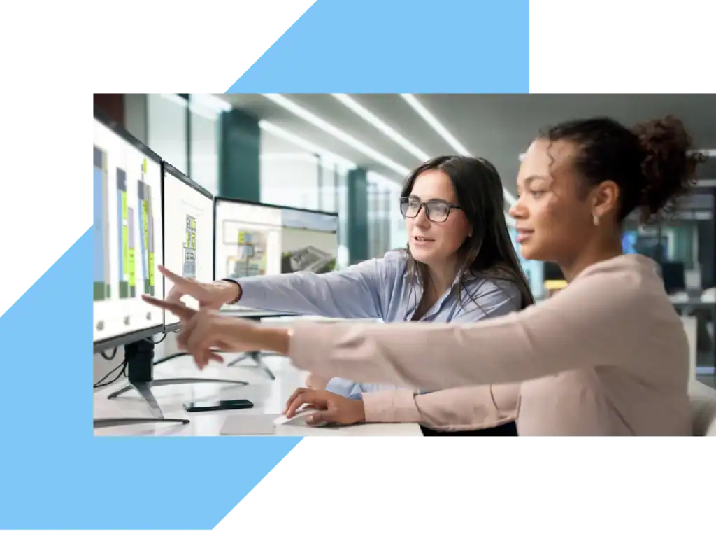 2 women sitting in front of a monitor who are pointing at it