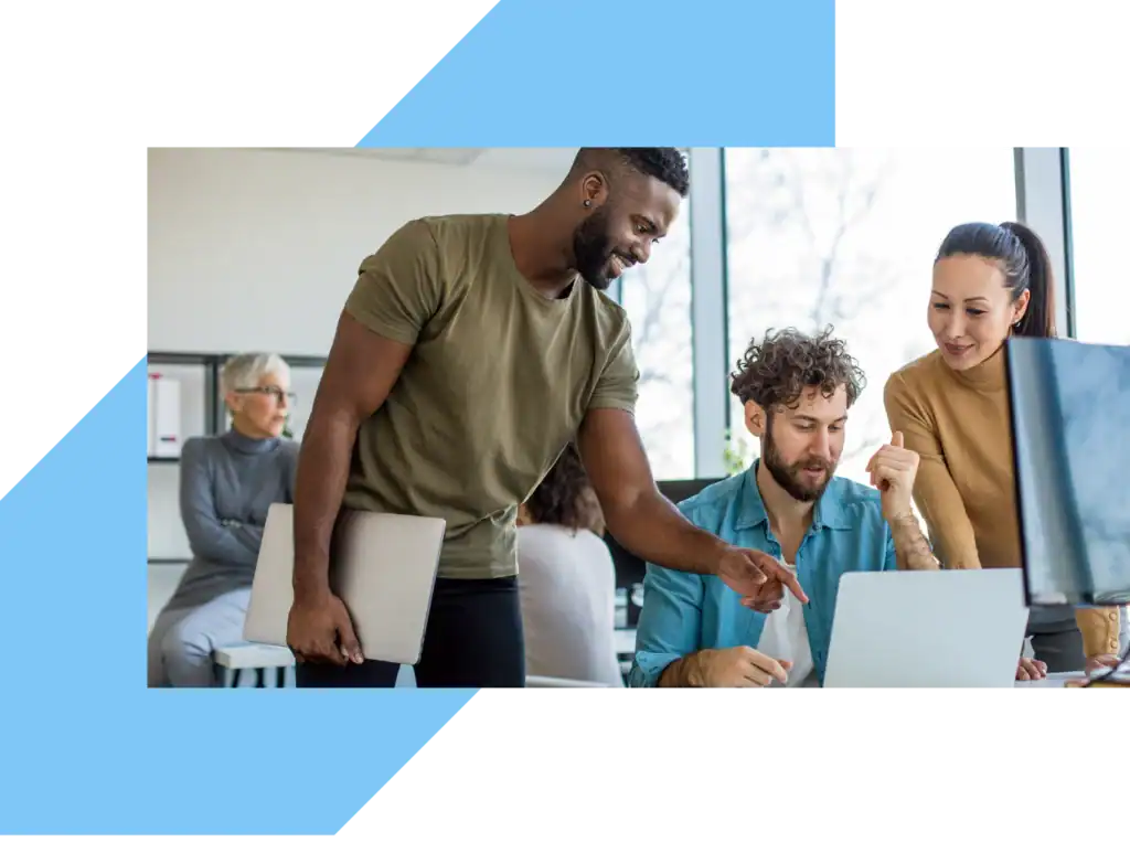 2 men and a women are standing at an office desk and looking at something on a laptop