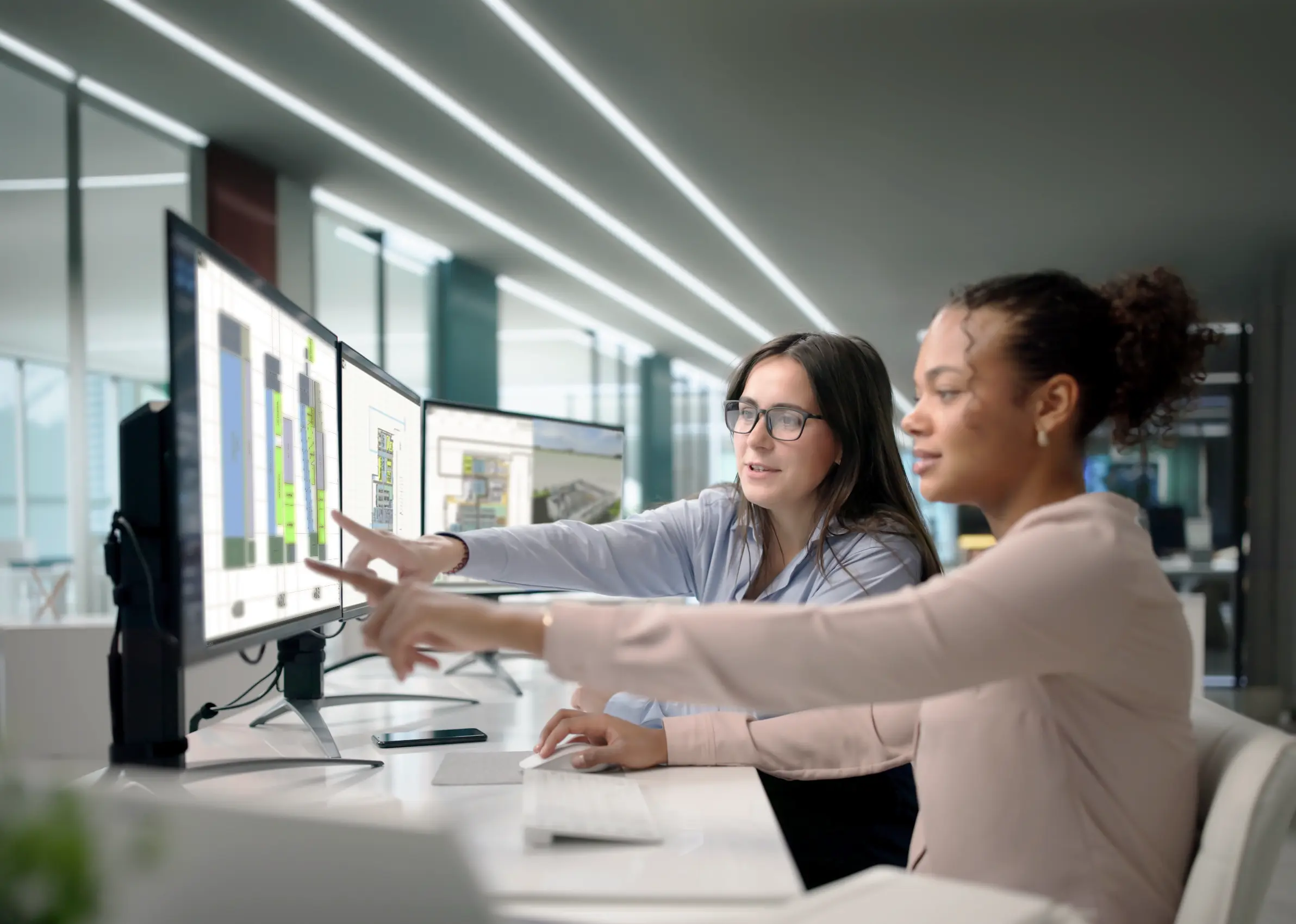 Two women sit at a desk with multiple screens and discussing layouts in visTable